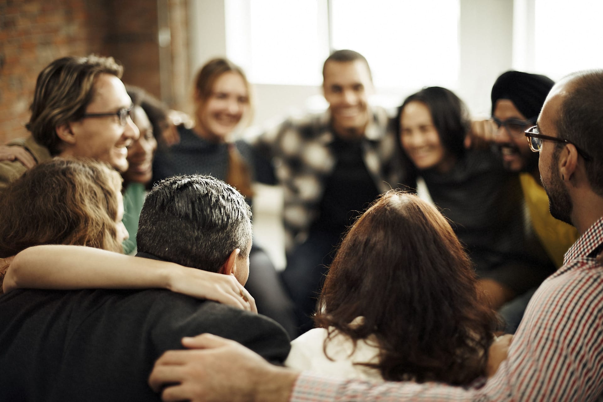 A group in a close huddle with their arms around each other’s shoulders, smiling